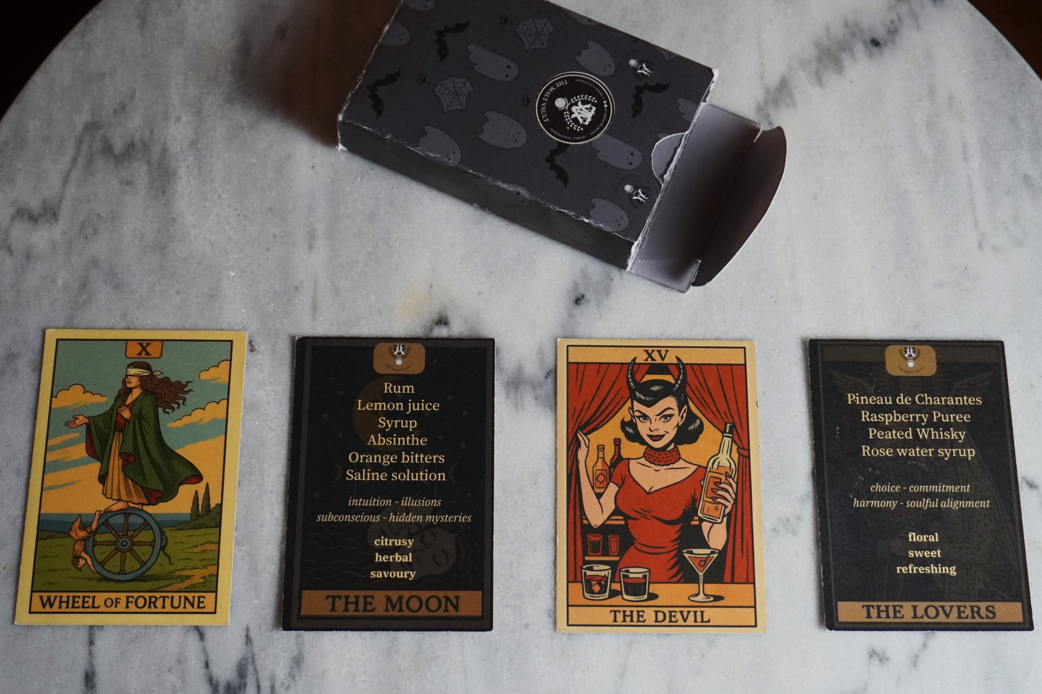 Tarot-inspired printed cocktail menu cards laid out on a marble table